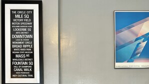 A living room with a patterned sofa, a framed list of street names, and a framed abstract art piece. - Broad Ripple 1 Bedroom  (Indianapolis)