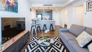 A modern living room with a flat-screen TV, a sofa, a coffee table, and a kitchen in the background. - 2BD Apt W/ Spectacular City Views/ Free carpark (South Brisbane)