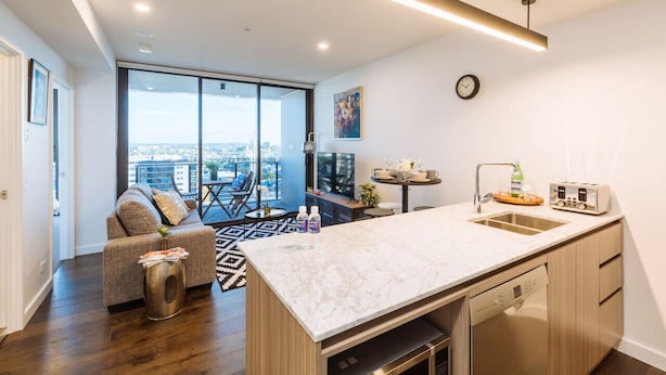 A modern kitchen with a large island, built-in dishwasher, and a view to the city. - 2BD Apt W/ Spectacular City Views/ Free carpark (South Brisbane)