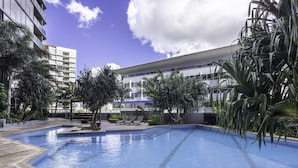 A modern hotel pool area with a clear blue pool, lounge chairs, and palm trees. - 2BD Apt W/ Spectacular City Views/ Free carpark (South Brisbane)
