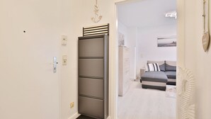 Ein Flur mit einem grauen Kleiderschrank, einer weißen Tür und Blick in ein Schlafzimmer mit einem grauen Sofa und einer weißen Wanddekoration.