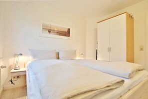 A bedroom with a bed, a nightstand, a lamp, a wardrobe, and a painting on the wall.