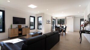 A modern living room with a black sofa, wooden furniture, a flat-screen TV, and a dining area with a table and chairs.