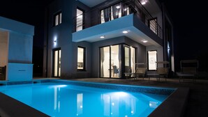 A modern two-story house with a swimming pool, large windows, and a balcony.