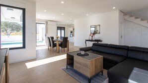 A modern living room with a black leather sofa, wooden coffee table, and a dining area with a table and chairs.