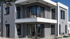 A modern two-story house with a balcony, large windows, and a flat roof.