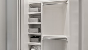 Ein weißer Kleiderschrank mit Regalen und Kleiderstange, der gefaltete Kleidung und Aufbewahrungsboxen enthält.