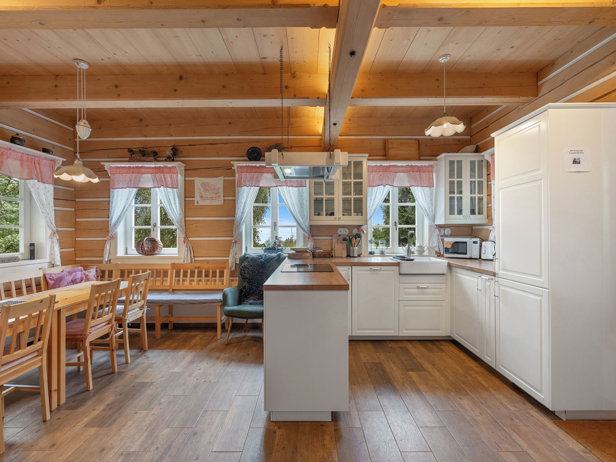 Een knus keuken in cottage-stijl met houten balken, een centraal eiland, witte kasten en een eethoek met houten meubilair.