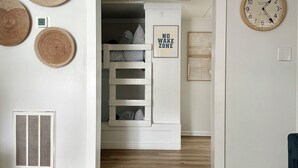 Une pièce avec un lit superposé, une horloge murale, un panneau indiquant une zone où il est interdit de faire du bruit et un tapis à motifs.