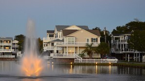 Une propriété située au bord de l’eau, dotée d’une fontaine centrale, de bâtiments à plusieurs étages avec des balcons, et d’un lac paisible qui reflète les constructions.