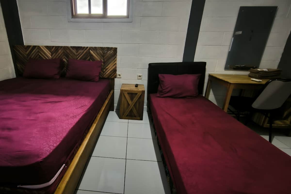 Een kamer met twee bedden, elk met een houten hoofdbord en een rode sprei. Er is een klein houten tafeltje met een stoel en een bureau met een stoel.