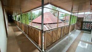 A covered outdoor area with a tiled floor, wooden railings, and a view of a red-roofed building in the background. - Pondok Kartini Jepara (Tahunan)