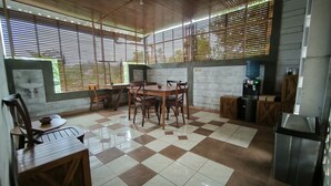 Een eetgedeelte met een geruite vloer, een houten tafel en stoelen. Achtergrond toont een spoelbak en een waterdispenser.