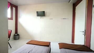 A room with two beds, a television mounted on the wall, and a trash bin.