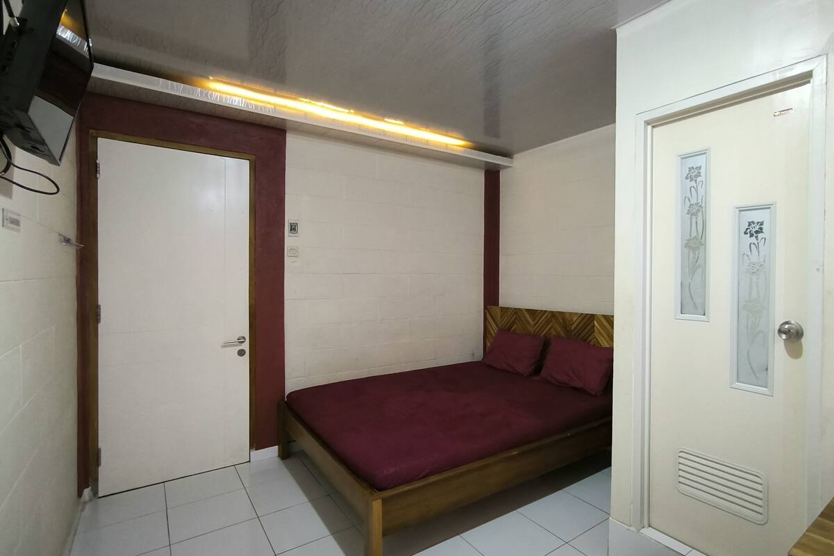 Een kleine kamer met een bed, een deur en een lamp.