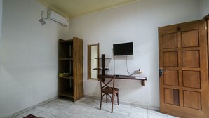 Een kamer met een houten bureau, een stoel, een aan de muur bevestigde televisie, een kledingkast en een deur.