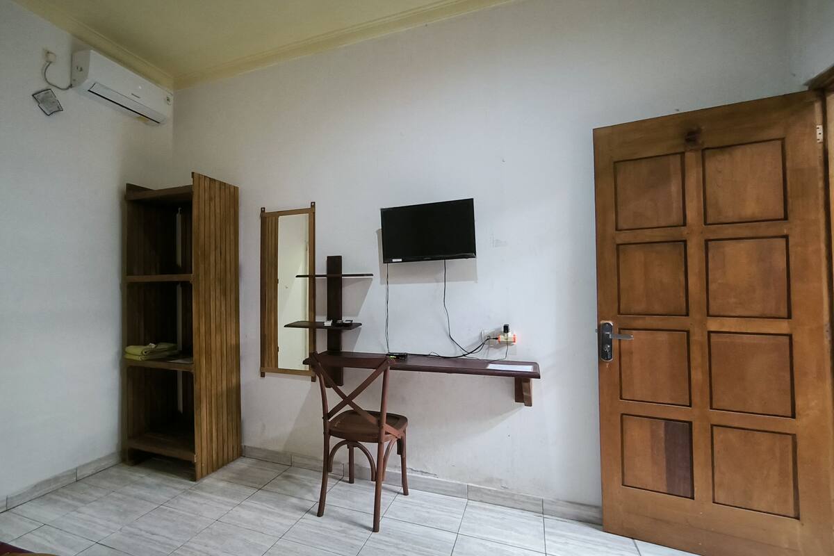 Een kamer met een houten bureau, een stoel, een aan de muur bevestigde televisie, een kledingkast en een deur.