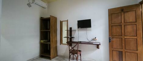 A room with a wooden desk, a chair, a television mounted on the wall, a wardrobe, and a door.