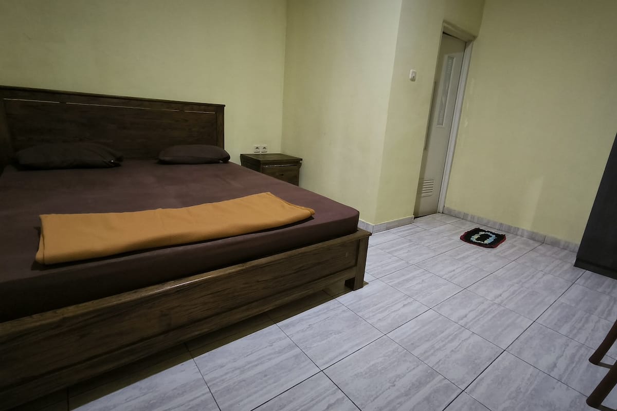 Een slaapkamer met een houten bed, een klein nachtkastje en een betegelde vloer.