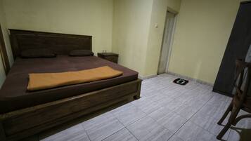Un dormitorio con una cama de madera, una mesita de noche pequeña y suelo de baldosas.
