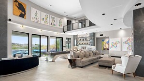 A modern living room with a curved sofa, a pool table, and artwork on the walls.
