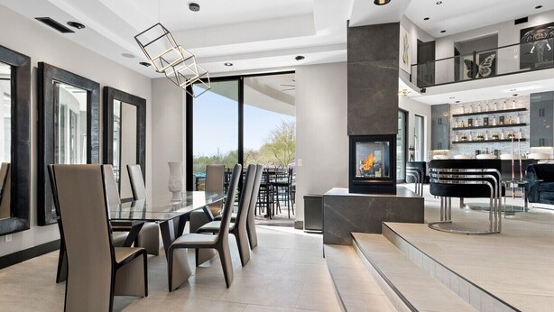 A modern dining area with a glass table and chairs, a fireplace, and a balcony with a view.
