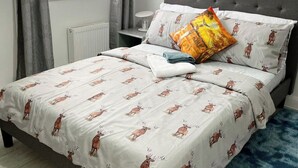 A bedroom with a bed featuring a deer print duvet and pillows, a bedside table with a lamp, and a window with curtains. - Apartment - Sleeps 4 - Parking - WiFi (Greater London, Dagenham)