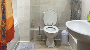 A bathroom with a toilet, bidet, sink, and a patterned shower curtain. - Apartment - Sleeps 4 - Parking - WiFi (Greater London, Dagenham)