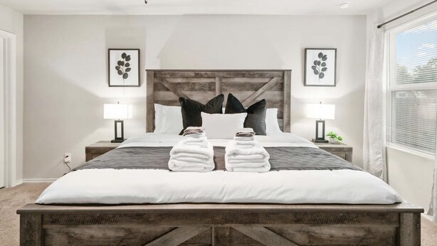 Un dormitorio moderno con una cama grande, cabecera de madera, dos mesitas de noche con lámparas y obras de arte enmarcadas en las paredes.