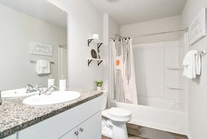 A modern bathroom with a granite countertop sink, a toilet, and a shower with a black and white striped shower curtain. - Serenity by Lackland: Family-sized home in San Antonio (San Antonio)