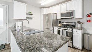 Una cocina moderna con armarios blancos, encimera de granito, electrodomésticos de acero inoxidable y un extintor en la pared.