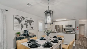 Una cocina moderna con electrodomésticos de acero inoxidable, un comedor con mesa blanca y platos negros, y un cuadro de un mapa mundial en la pared.
