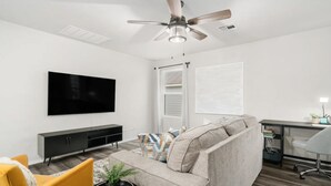 Una sala moderna con un sofá gris, un sillón amarillo y un mueble de televisión negro.