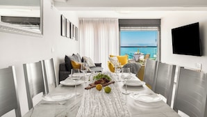A dining area with a table set for four, a view of the sea through a window, and a flat-screen TV mounted on the wall. - Sea of Galilee Panorama Apt by SeaN'Rent (Tiberias)