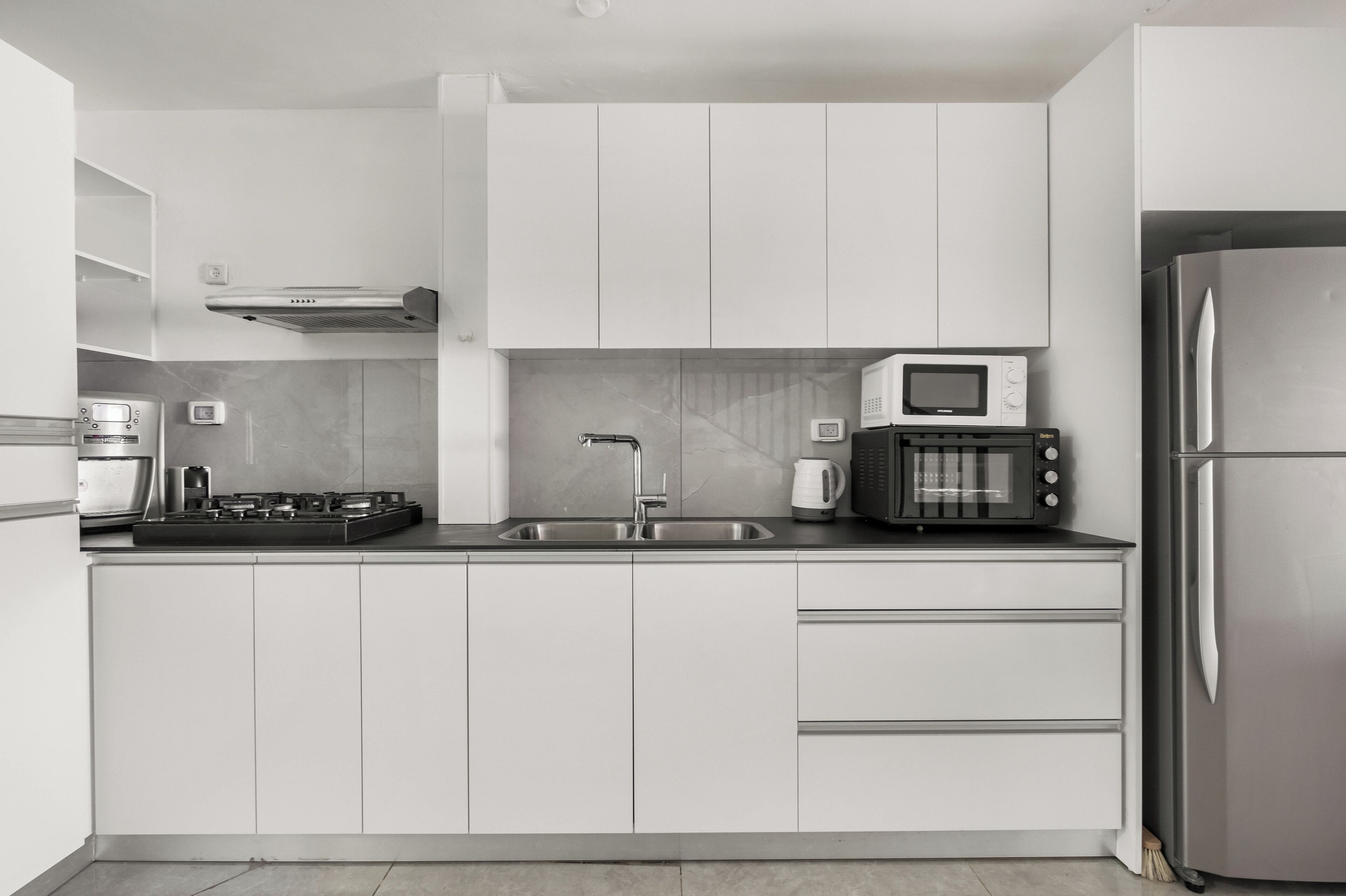 A modern kitchen with white cabinets, a stainless steel refrigerator, a microwave, a toaster, and a gas stove.