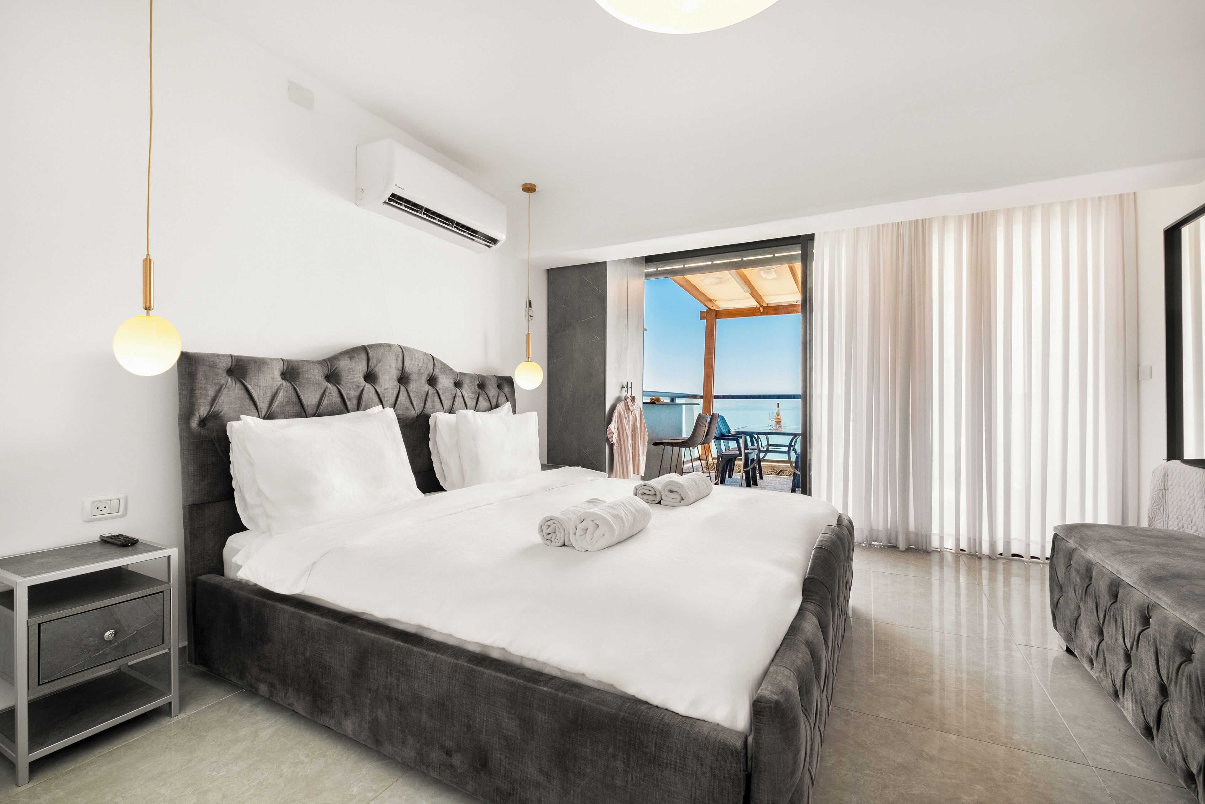A modern hotel room with a large bed, a nightstand, and a view of the sea through a balcony.