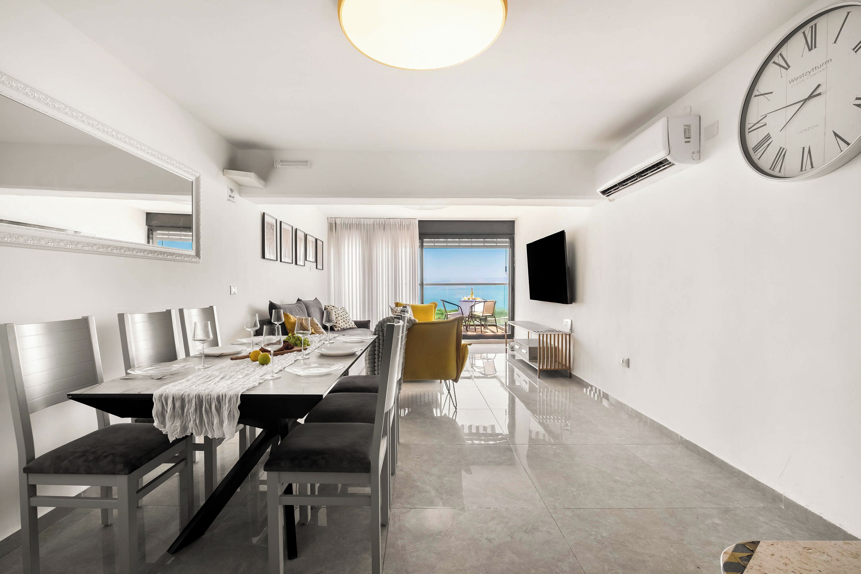 A modern dining area with a long table, chairs, and a television mounted on the wall.