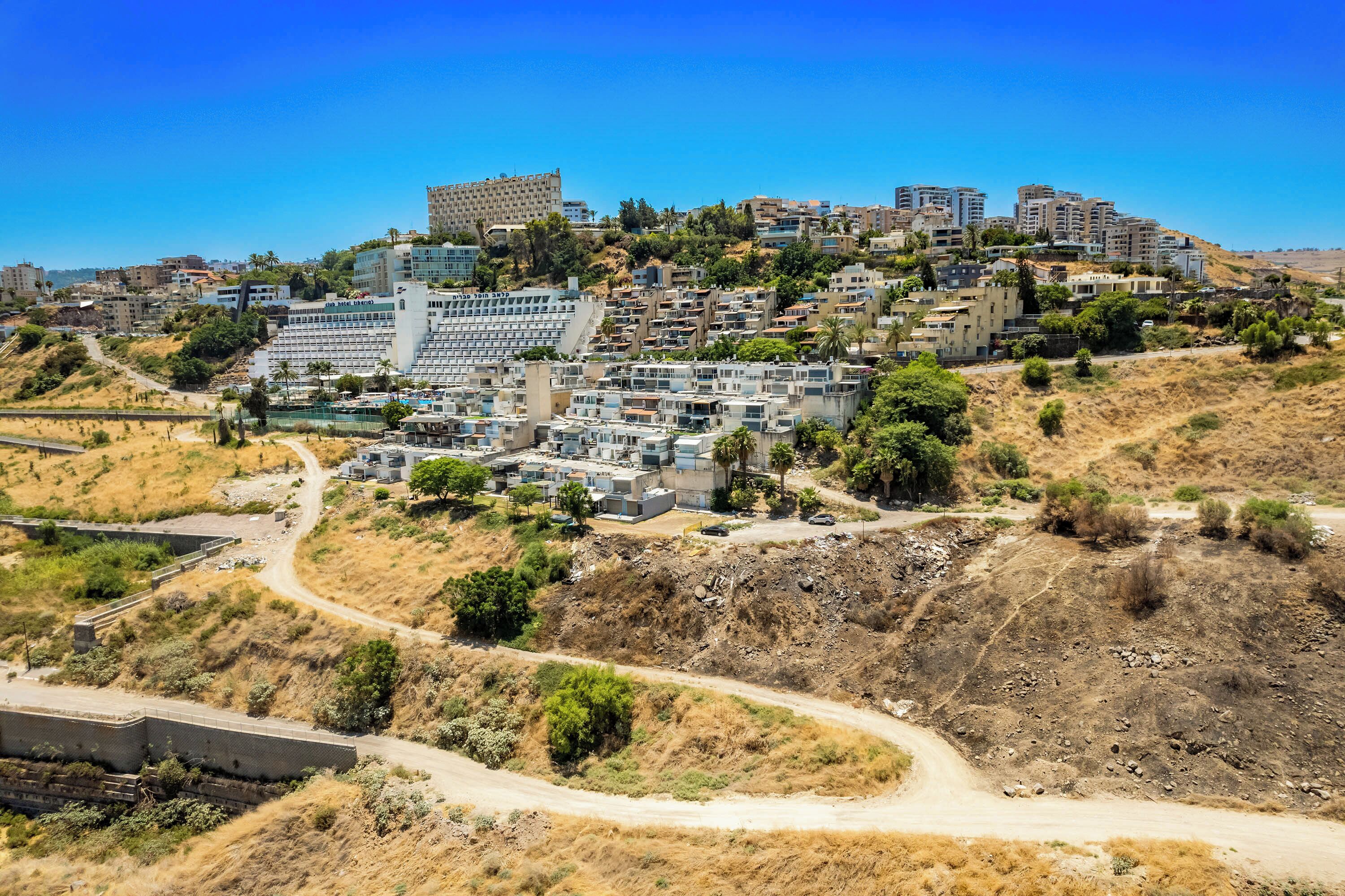 Un barrio residencial en una ladera con edificios modernos, un camino de tierra y vegetación escasa.