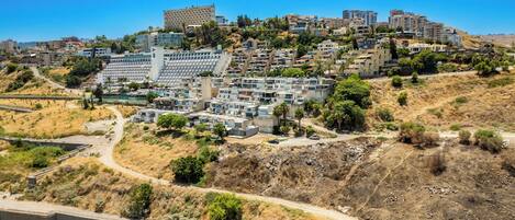 Un barrio residencial en una ladera con edificios modernos, un camino de tierra y vegetación escasa.