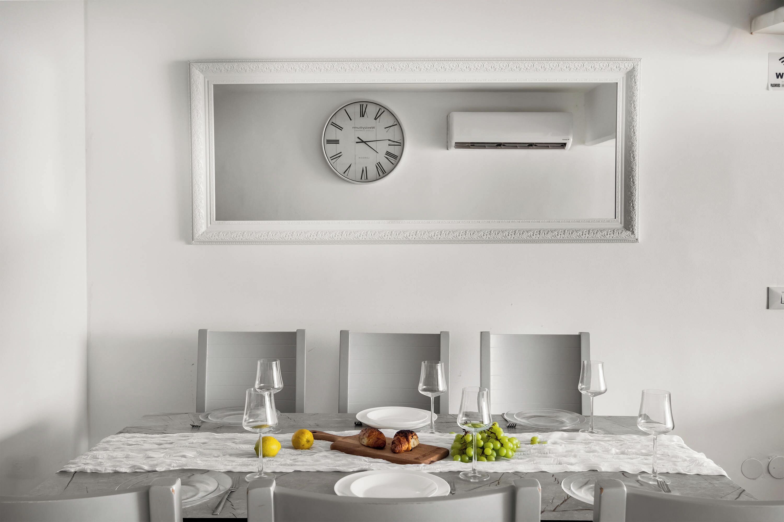 A dining area with a table set for four, a clock, and an air conditioning unit on the wall.