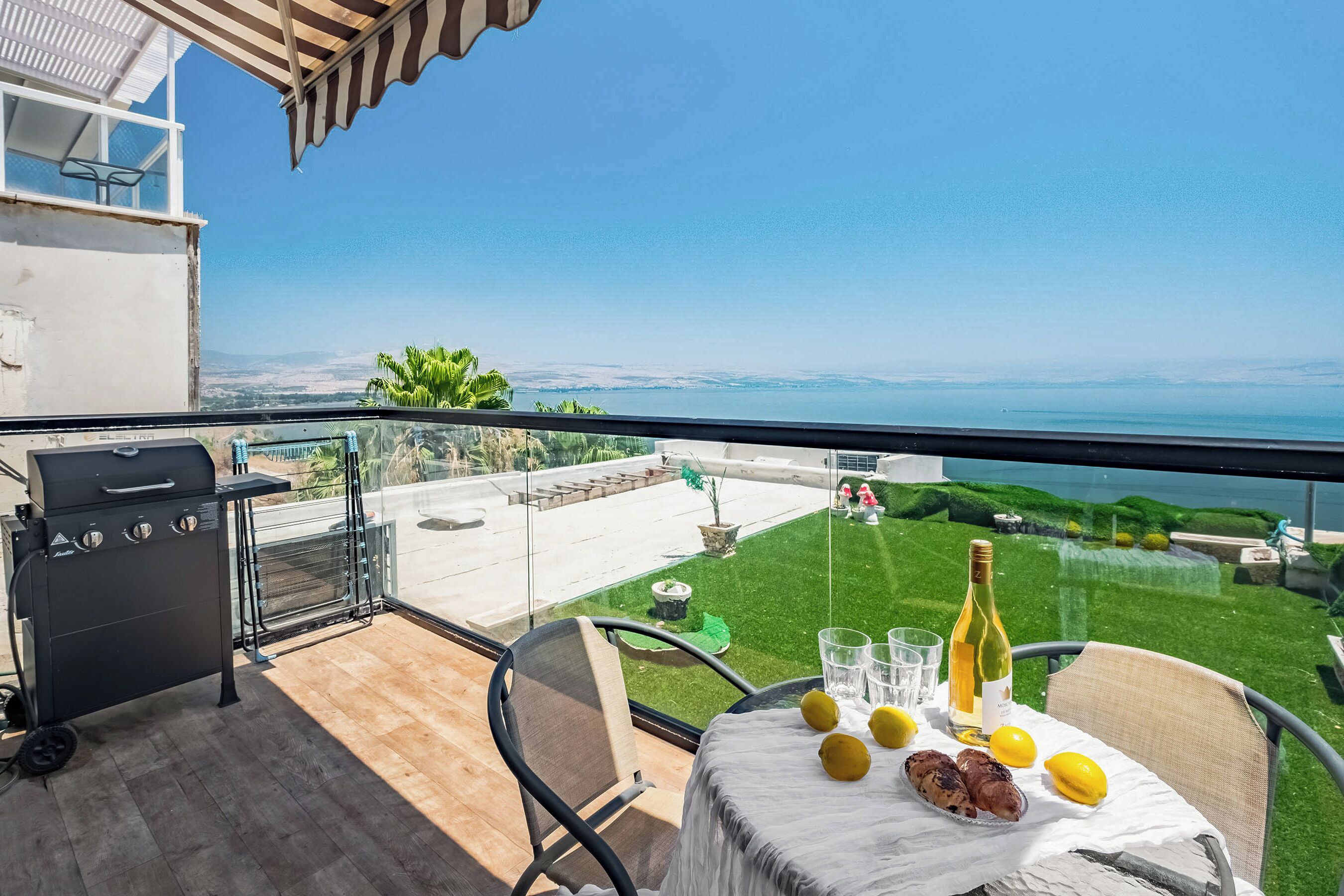 A balcony with a grill, table with lemons and a bottle, and a view of the sea.