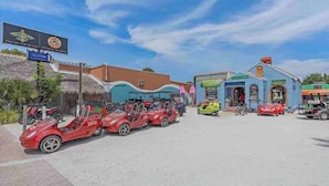 A parking area with several red toy cars, a blue building with a sign, and a clear sky. - Siesta Key Village • Pool • Walk to Beach • Pets (Sarasota)
