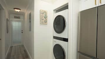 Un pasillo con una puerta, una lavadora empotrada en la pared y un refrigerador.