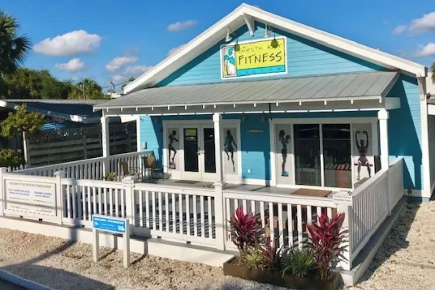 A fitness center with a blue exterior, a covered entrance, and a fenced outdoor area.