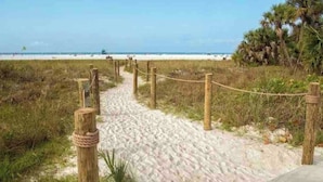 A sandy beach path with wooden posts and rope barriers, leading to a beach with palm trees and the ocean in the background. - Siesta Key Village • Pool • Walk to Beach • Pets (Sarasota)