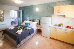 A hotel room with a bed, a small kitchenette, and a view of the outside.