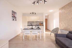 A modern kitchen with white cabinets, a dining table set for four, and a chandelier above.