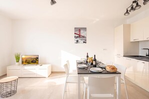 A modern kitchen with white cabinetry, a dining area with a table set for two, and a kitchen island with a plant.