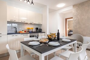 Une cuisine moderne avec des meubles blancs, une table à manger dressée pour quatre personnes et une vue sur une chambre.