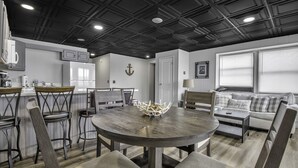 A modern kitchen with a dining area, a living room with a sofa, and a ceiling with a grid pattern. - FLX Retreats Conesus Condos- APT B (Geneseo)